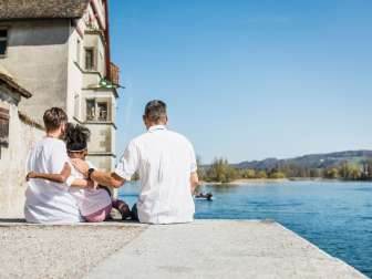 La mère et le père sont assis avec leur fille sur un mur de pierre au bord du Rhin.