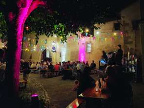 nordArt Stein am Rhein Bancs de fête dans une cour intérieure illuminée. Les bancs sont remplis de gens. Une kleine Bühne installée. Un musicien y joue de la musique.