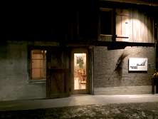 La façade d'une ancienne grange. On aperçoit des sièges à travers la porte. Sur le côté droit de l'entrée, il y a un panneau sur lequel on peut lireHirschen Bühne".