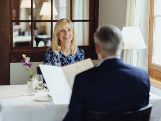 Deux personnes sont assises à une table dressée d'une nappe blanche et consultent le menu.