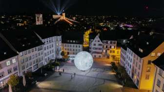 Vue d'en haut, de nuit, sur le Munot illuminé. Des faisceaux de lumière brillent dans le ciel nocturne.