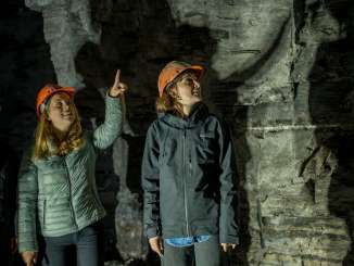 Trois personnes se trouvent dans une galerie de montagne. Elles portent toutes un casque. L'une d'elles pointe le plafond de l'index.