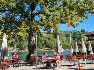Terrasse du restaurant Unterhof Des tables et des chaises rouges ainsi que des parasols blancs sont installés sur une terrasse au bord du Rhin.