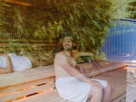 Des personnes sont assises dans un sauna. Des feuilles de bambou se reflètent dans le verre.