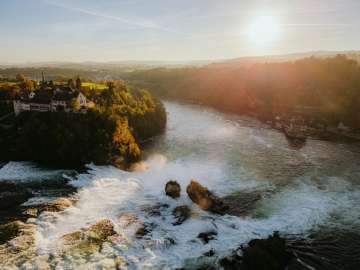 Vue d'en haut sur les deux rochers de la chute d'eau, à gauche le Schloss Laufen et à droite le Schlössli Wörth. La lumière dorée du soir brille sur la chute d'eau.