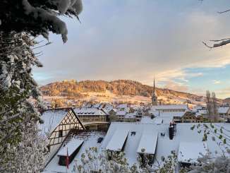 Vue sur la vieille ville de Stein et le château de Hohenklingen. Les toits des maisons sont recouverts de neige et le soleil couchant projette une lumière dorée.
