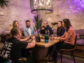 Un groupe est assis à une table en bois. Il y a un plateau d'apéro et différentes bouteilles de gin à déguster.