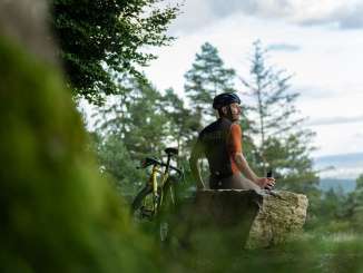 Un cycliste est assis sur un gros rocher et fait une pause pendant son parcours sur gravier.