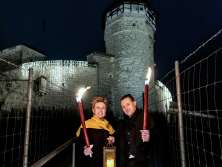 Un homme et une femme se tiennent devant la forteresse Munot, chacun tenant une torche allumée. Elle tient également une lanterne avec une bougie.