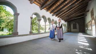 Deux femmes déguisées en huguenots se promènent dans le cloître de Schaffhouse. L'une porte un tablier bleu et l'autre un tablier violet.