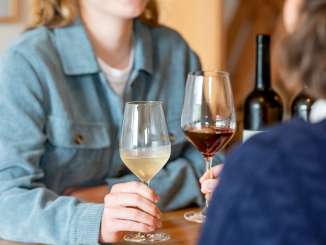 Deux amies sont assises à une table en bois. Une femme tient un verre de vin blanc et l'autre un verre de vin rouge.