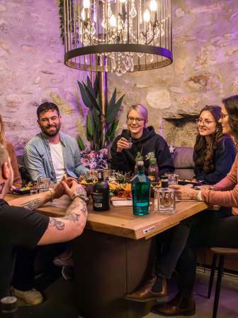 Un groupe est assis à une table en bois. Il y a un plateau d'apéro et différentes bouteilles de gin à déguster.