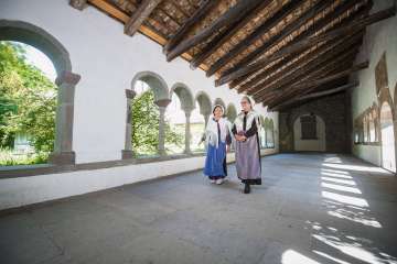 Deux femmes déguisées en huguenots se promènent dans le cloître de Schaffhouse. L'une porte un tablier bleu et l'autre un tablier violet.