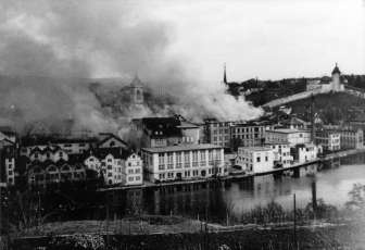 Une vieille image en noir et blanc d'une ville. Des nuages sombres s'élèvent au-dessus de la ville.