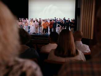 Municipal theatre de Schaffhouse Spectacle avec public Une scène de théâtre avec de très nombreux artistes. Dans la salle, des spectateurs sont assis sur les sièges rouges.