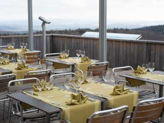 Terrasse du Randenahus de Siblingen Une terrasse en bois est équipée de tables et de chaises couvertes. On a une vue lointaine jusqu'aux Alpes suisses.