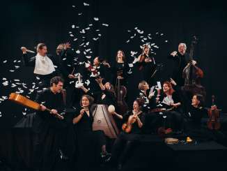 Plusieurs musiciens vêtus de noir se tiennent devant un fond noir, un instrument à la main, tandis que des plumes blanches virevoltent dans les airs.
