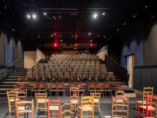 Une scène avec de nombreuses chaises en bois différentes. Une tribune avec des chaises. L'entrée se trouve à droite.
