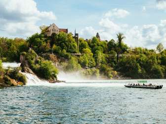 Un bateau vert se dirige vers les chutes d'eau dans le bassin des chutes du Rhin. De nombreuses personnes se trouvent à bord.