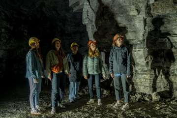 Cinq amies portent des casques jaunes et orange. Elles se tiennent dans une ancienne galerie de plâtre.