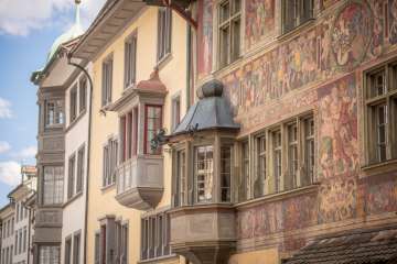 oriel Haus zum Ritter Vue de plusieurs façades de maisons avec un oriel. L'une des façades est légèrement jaune, l'autre richement décorée de peintures.