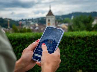 Foxtrail GO Schaffhouse Une main tient un téléphone portable. On y voit l'énigme numérique Foxtrail GO.