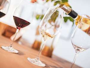 Il y a quatre verres à vin sur une table. Deux d'entre eux sont remplis de vin rouge, un est vide et un vin blanc est versé dans un verre.