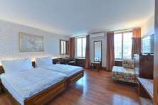 Chambre double de l'hôtel Rheinfels. Sur un sol en bois sombre se trouve un lit double avec des draps blancs. Les murs sont recouverts d'un papier peint à fleurs.