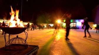 Ein Eisfeld bei Nacht wird beleuchtet. Personen laufen Schlittschuh.