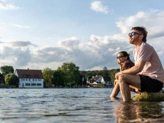 Deux personnes sont assises sur de gros rochers dans le Rhin et se rafraîchissent les pieds dans l'eau.