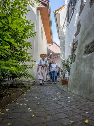 Visite guidée de Hallau Un groupe accompagné d'un guide en costume traditionnel se promène dans une ruelle très étroite.