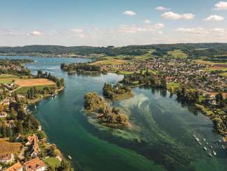 Vue d'en haut sur l'Untersee, aux eaux vertes et turquoise, avec l'île de Werd. Le long des rives s'étendent de petits _villages et un paysage verdoyant.