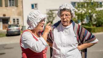 Visite guidée "Wöschwiiber" à Wilchingen Deux maîtresses vêtues d'une robe et d'un bonnet blanc "papotent" ensemble.
