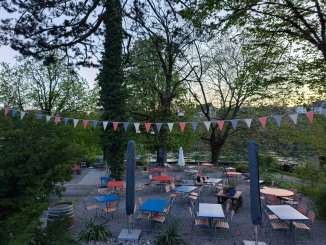 Carcajou Jardin de la vallée du Rhin Des tables et des chaises bleues et rouges sont installées sur une terrasse au bord du Rhin.