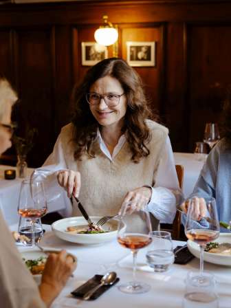 Drei Freundinnen sitzen an einem weiss gedeckten Tisch. Darauf stehen Weingläser mit Rosé und ein Fischmenü.