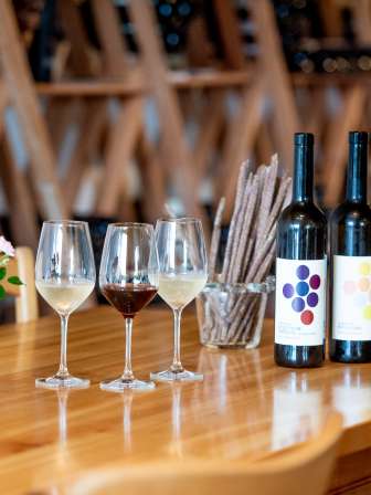 Sur une table en bois, il y a des grisini, une fausse bouteille de vin rouge et une fausse bouteille de vin blanc, ainsi que deux verres à vin blanc et un verre à vin rouge.