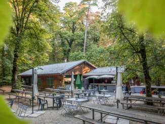 Mitten im Wald steht ein Restaurant in einer Hütte mit vielen Tischen draussen.
