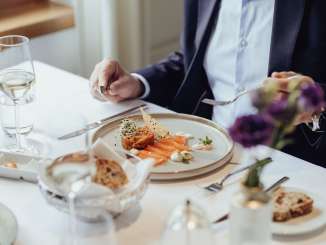 Sur une table nappée de blanc, il y a une entrée de saumon ainsi qu'un verre de vin blanc et du pain.