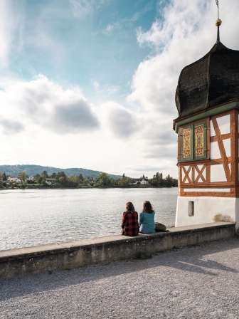 Pause randonnée à Stein am Rhein Deux amies sont assises au bord du Rhin et font une pause. Sur leur gauche se dresse une petite tour en forme de barre avec un toit en bulbe.