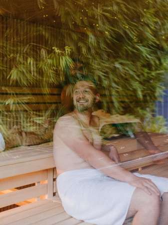 Des personnes sont assises dans un sauna. Des feuilles de bambou se reflètent dans le verre.
