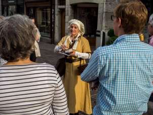 Visite guidée "Odeurs médiévales Un guide habillé d'une robe jaune et d'une cagoule se tient devant un groupe.