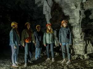 Cinq amies portent des casques jaunes et orange. Elles se tiennent dans une ancienne galerie de plâtre.