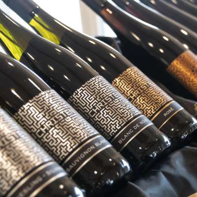 Mehrere Weinflaschen liegen auf einem Tuch. Die Etiketten sehen wie ein Labyrinth-Muster aus.