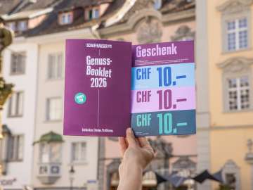 Eine Person hält das Genuss-Booklet in die Luft. Eine Broschüre mit Genusstipps und Gutscheinen zum Einlösen.