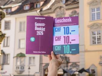 Eine Person hält das Genuss-Booklet in die Luft. Eine Broschüre mit Genusstipps und Gutscheinen zum Einlösen.