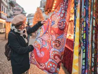 Une femme porte un manteau d'hiver et un béret et regarde une écharpe colorée à un stand de Noël.