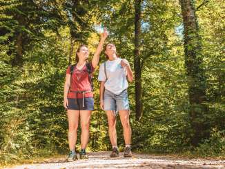 Deux amies en tenue de randonnée se trouvent dans la forêt. La femme au t-shirt rouge montre quelque chose du doigt.