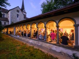 Divers stands de dégustation de vin sont installés dans le cloître de Allerheiligen . Des personnes se tiennent debout devant les stands et boivent du vin.