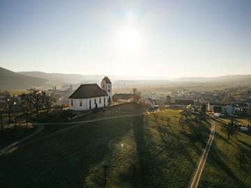 Auf einem Hügel steht eine Kirche. Dahinter sieht mein ein kleines Dorf.