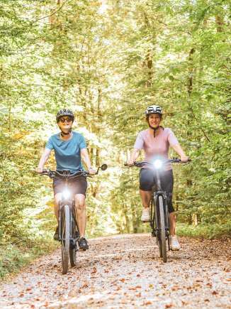 Zwei Freundinnen fahren mit ihrem E-Bike auf einem Naturweg durch den Wald.